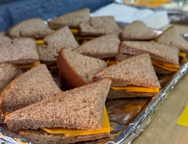 Halved whole grain bread and sliced cheese sandwiches on a silver tray.