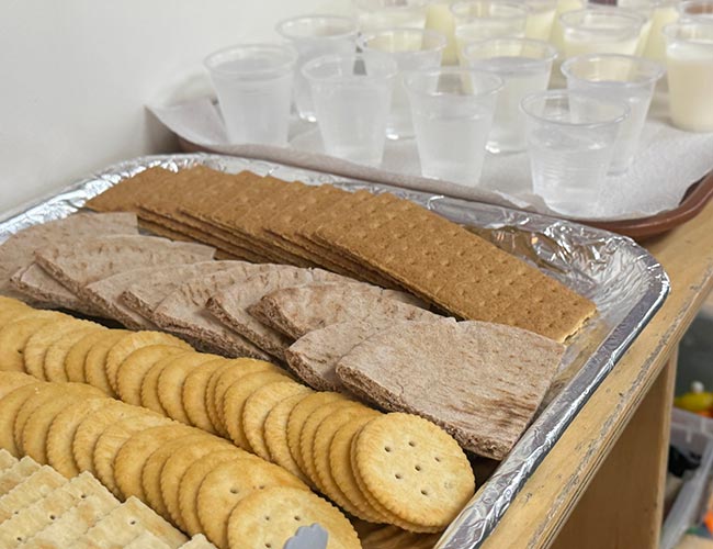 Trays of whole grain crackers and pita bread alongside cups of fresh milk and water.
