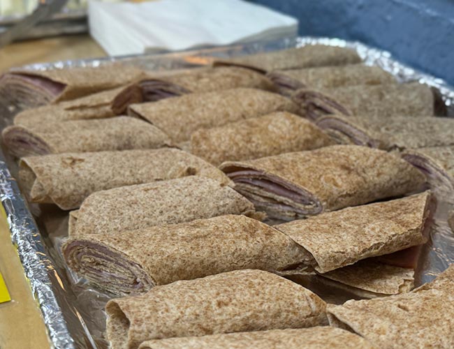 Sliced whole wheat tortilla wraps filled with turkey and cheese on a catering tray.